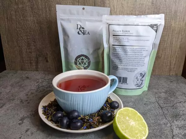 Blueberry and lime juice and so many other delicious flavours in this RPG inspired tea. One cup of tea on a saucer, with blueberries and lime and two examples of packaging.