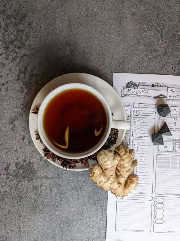 Masala chai tea from the top with ginger and a character sheet for Dungeons and Dragons with stone dice